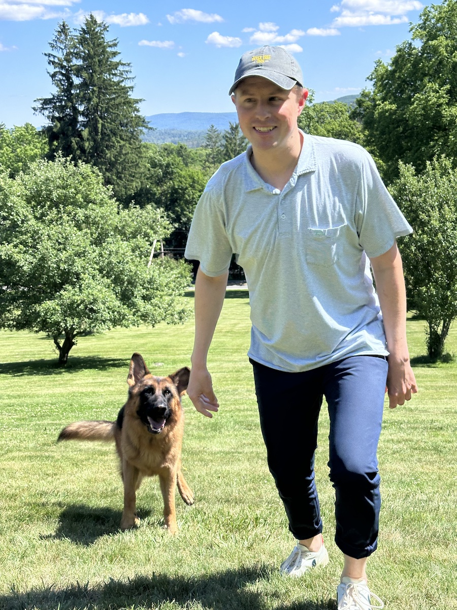 Christian and his German shepherd Max climing the hill, with two of our actual surviving apple trees in the background, Christian in an Apple Tree branded baseball cap, Max following attentively behind